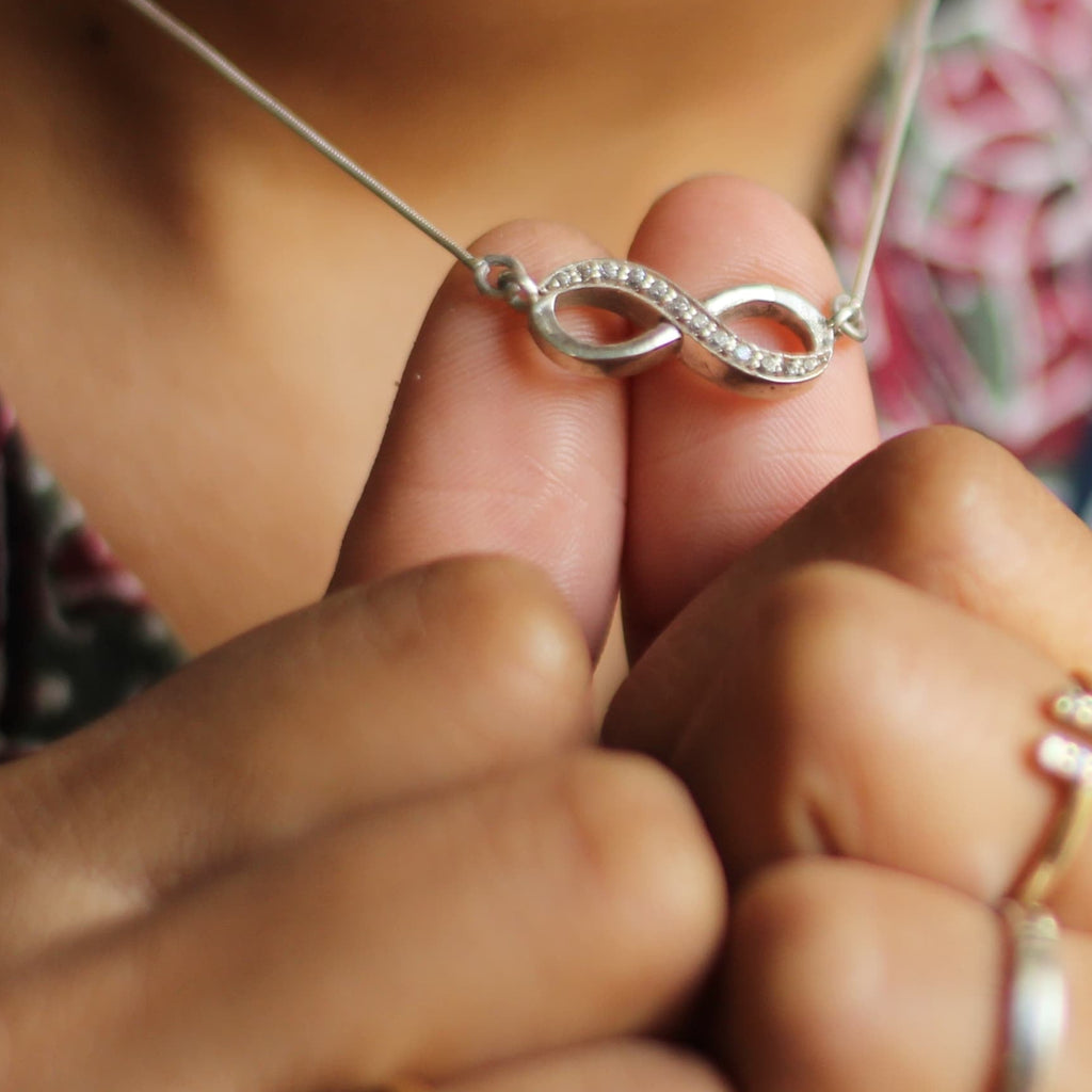 A person holding a silver pendant with an infinity symbol design, attached to a chain.